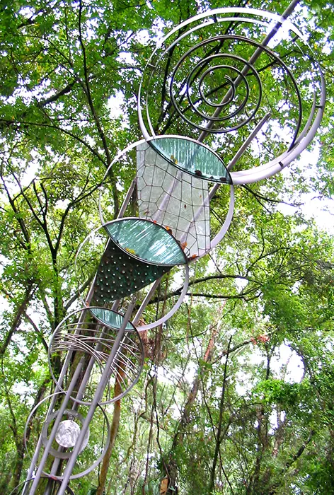 A tree with two metal sculptures hanging from it.